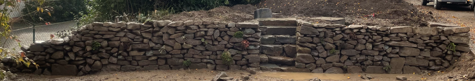 Trockenmauer Grauwacke Trockenmauer aus Grauwacke mit integrierter Treppenanlage und Bepflanzung. Länge: 14m. Dient der Terassierung.
